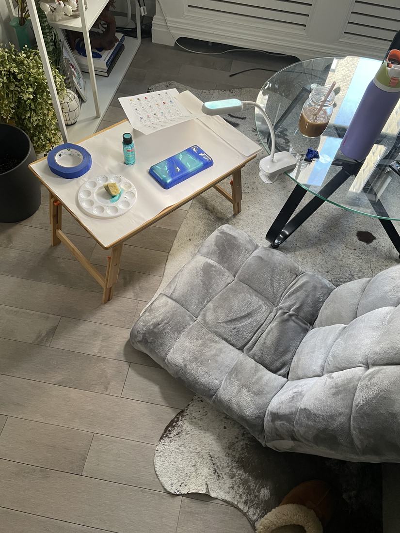 A cozy living room corner with a small craft table, supplies, and a plush grey chair.
